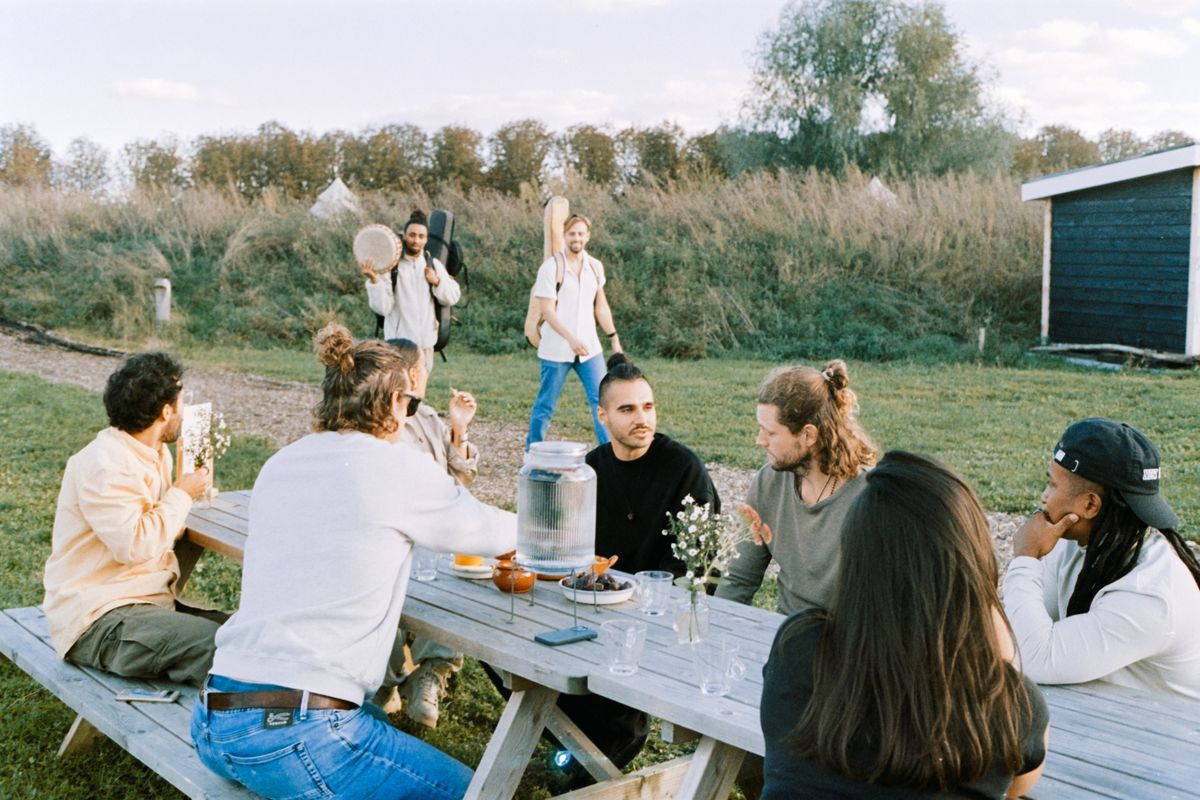 A team talking around a wooden table in a field, flowers and a water jar between them.