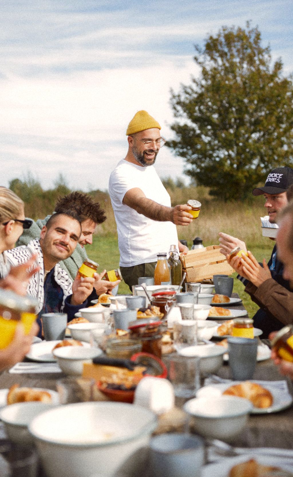 Garo Feslian raising a glass at a long breakfast table in a field.