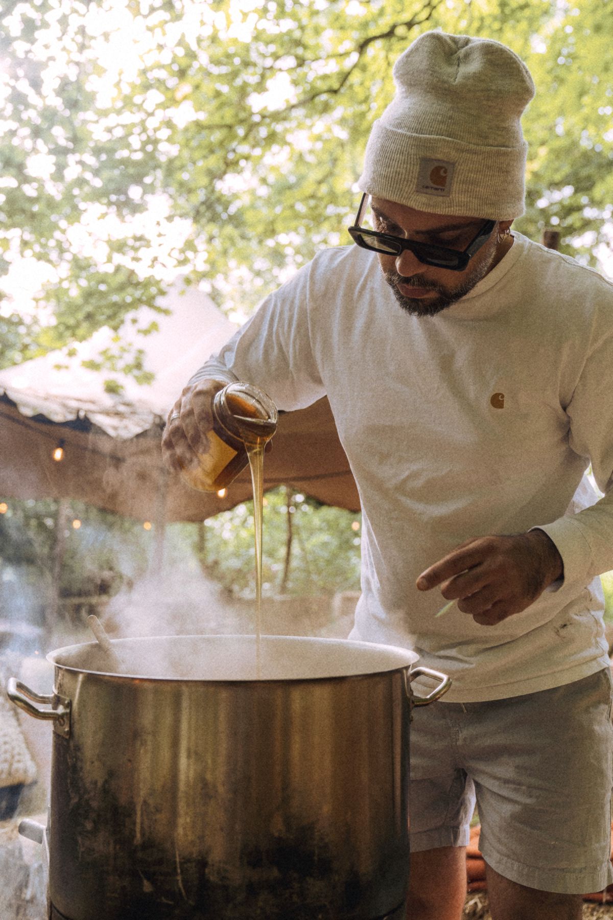 Garo pouring oil into a steaming pot in the open-air kitchen.