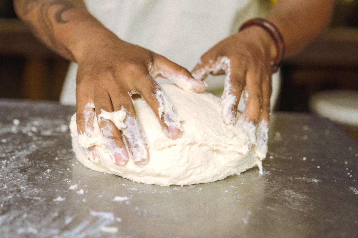 Floury hands kneading a large dough on a steel table.