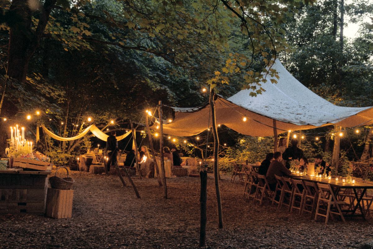 Dinner under string lights and a canvas roof in the forest.