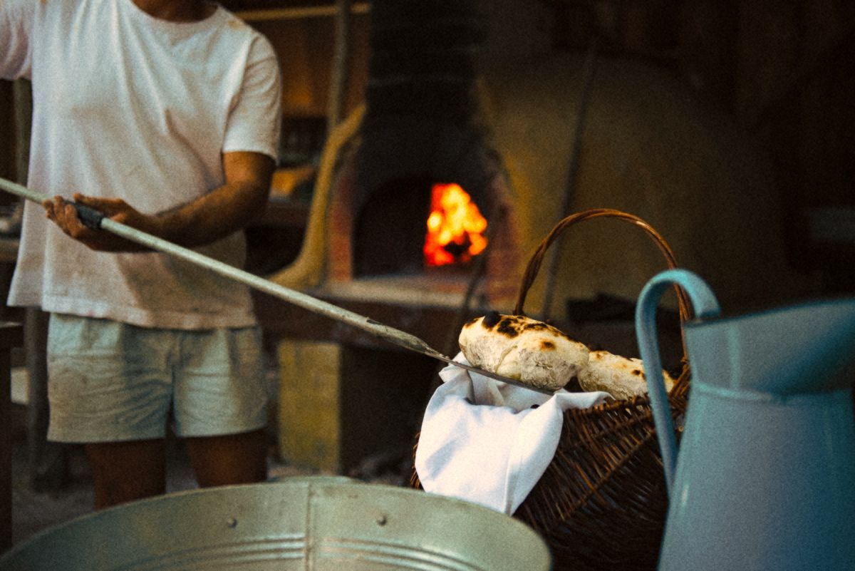 Bread coming out of the wood-fired oven on a long peel, into a basket.